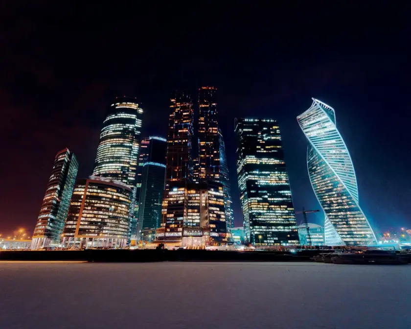 Gratte-ciels modernes illuminés la nuit, reflétant une ambiance urbaine dynamique.