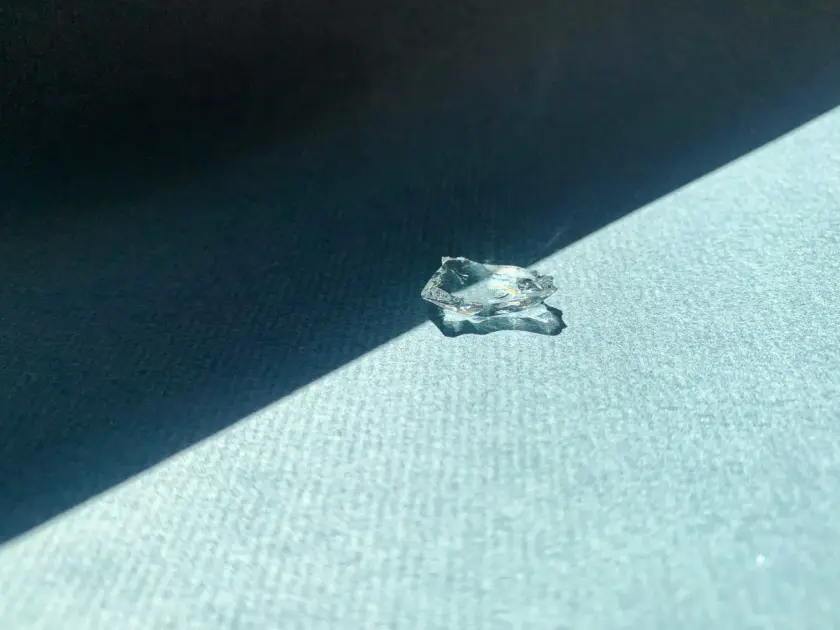 Un morceau de verre transparent posé sur une surface texturée, éclairé par un rayon de lumière.