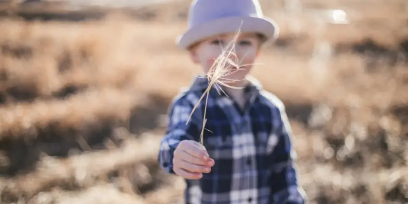 Un enfant portant un chapeau tient une tige d'herbe dans un champ sec.