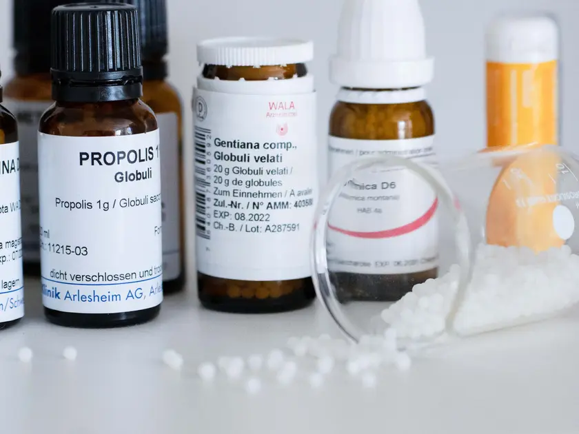 Flacons de médicaments homéopathiques avec étiquettes, certains renversés et des granules dispersés.