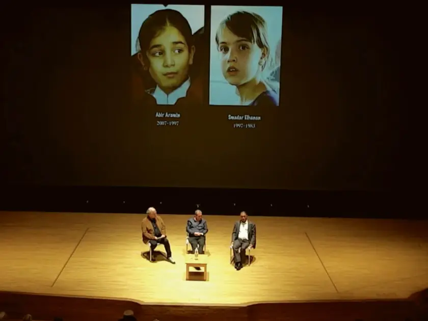 Deux portraits d'enfants projetés sur un écran, avec trois personnes assises sur scène.