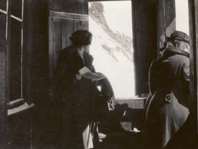 Deux personnes à l'intérieur d'un bâtiment, regardant par une fenêtre ouverte vers un paysage montagneux.