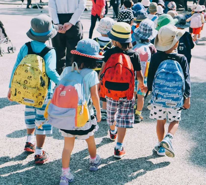 Groupe d'enfants marchant en file, portant des chapeaux et des sacs à dos colorés.