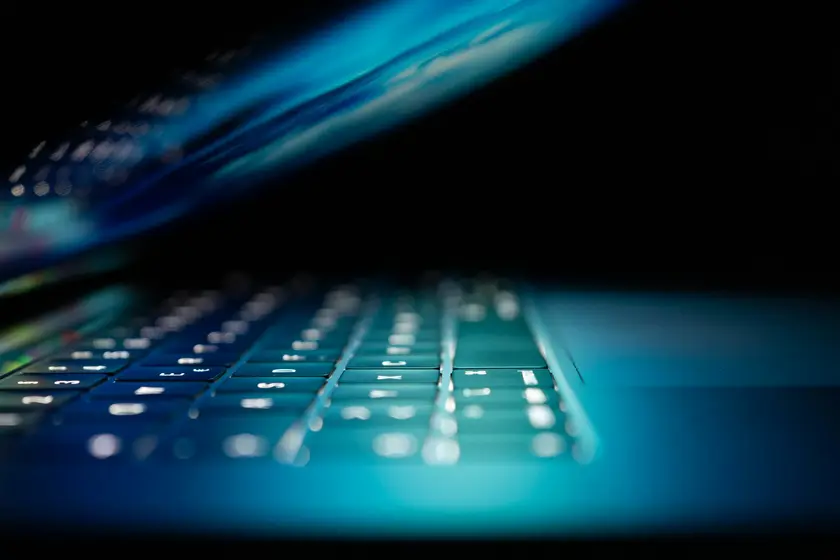 Clavier d'ordinateur portable illuminé, avec un écran légèrement incliné, sur fond sombre.